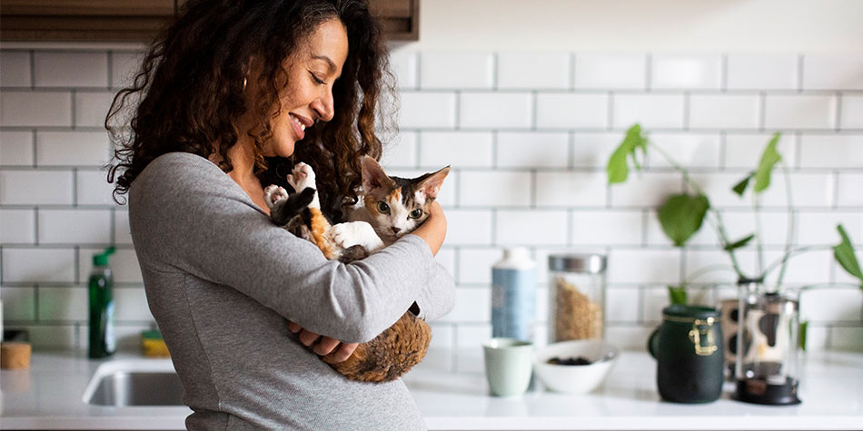 Expectant mom holds a cat and smiles in her kitchen.